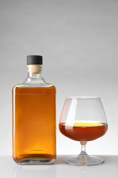 Bottle and glass with whiskey on white table against light background