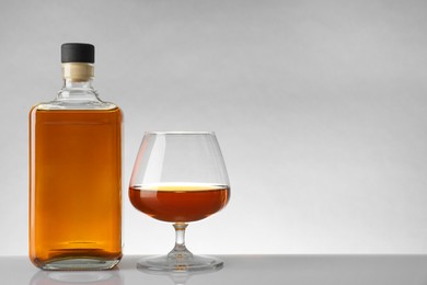 Photo of Bottle and glass with whiskey on white table against light background, space for text