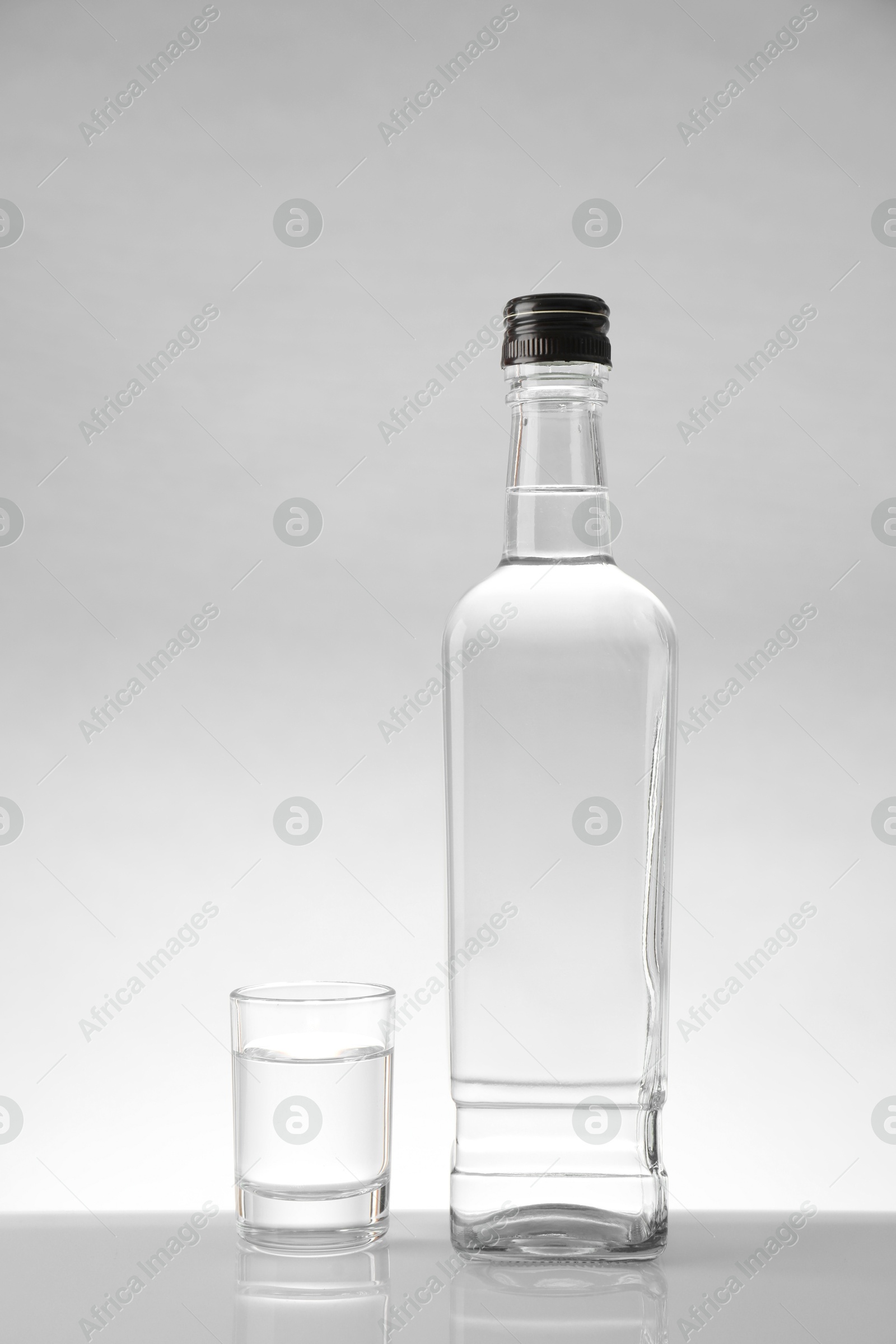 Photo of Bottle and glass with vodka on white table against light background