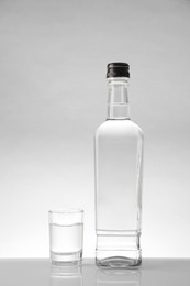 Photo of Bottle and glass with vodka on white table against light background