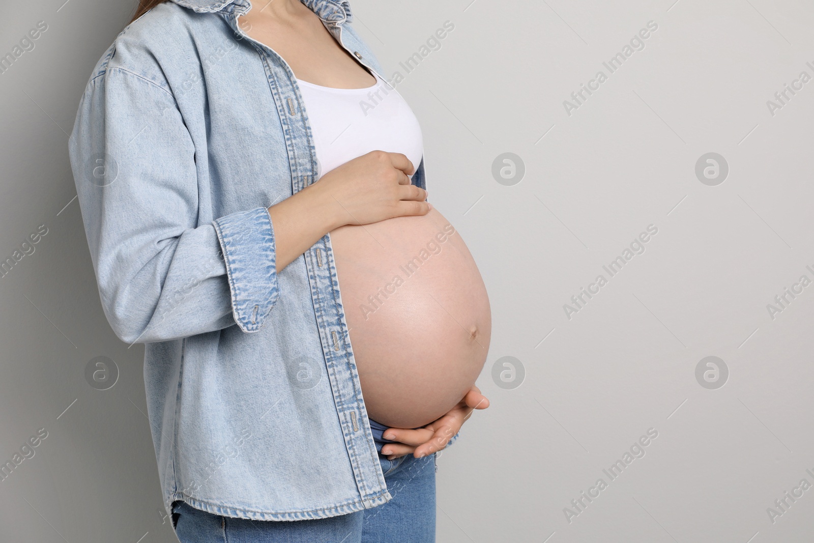 Photo of Pregnant woman on gray background, closeup. Space for text