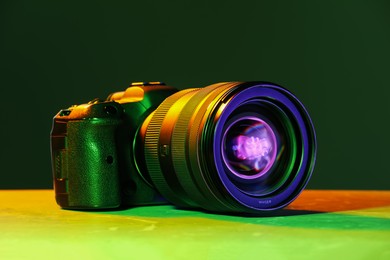 Photo of Modern photo camera in neon lights on table