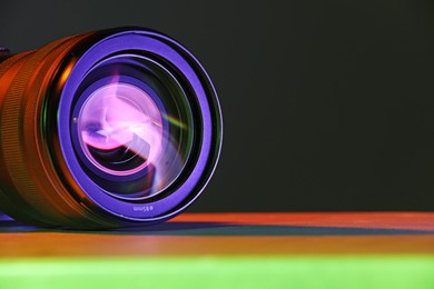 Modern camera lens in neon lights on table, closeup. Space for text