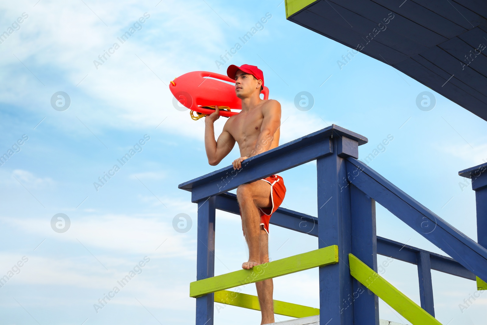 Photo of Handsome lifeguard with life buoy on watch tower against sky