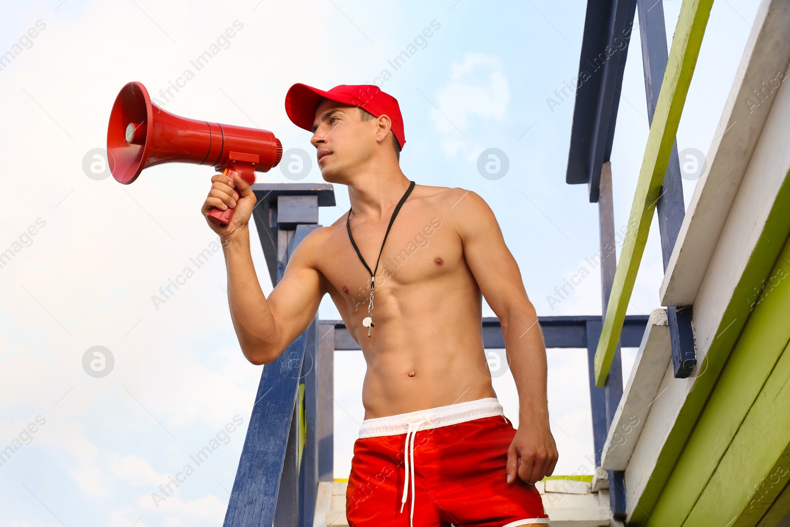 Photo of Handsome lifeguard with megaphone on watch tower against sky