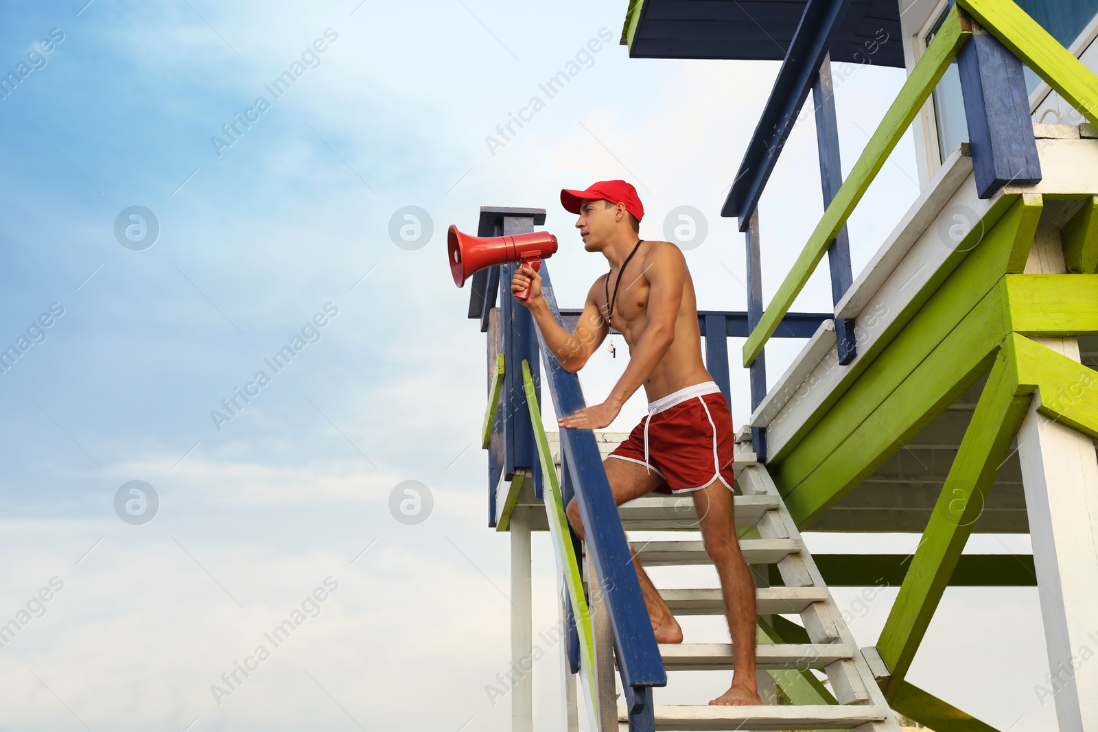 Photo of Handsome lifeguard with megaphone on watch tower against sky