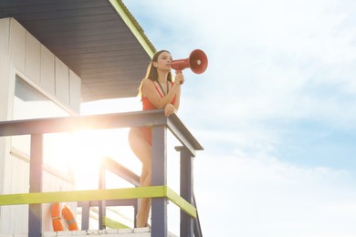 Beautiful young lifeguard with megaphone on watch tower against sky