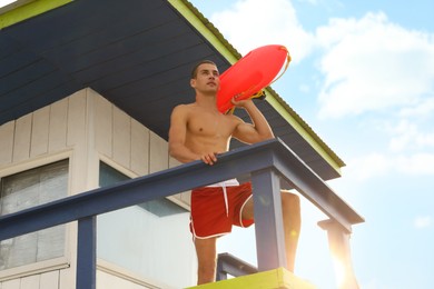 Photo of Handsome lifeguard with life buoy on watch tower, low angle view