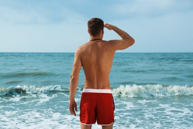 Photo of Handsome lifeguard near sea on summer day, back view