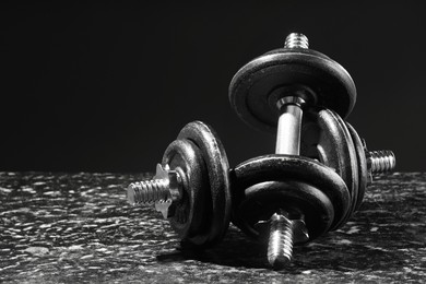 Two barbells on grey textured table against black background, closeup. Space for text