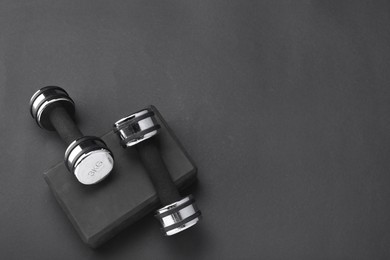 Two dumbbells and yoga block on black background, flat lay. Space for text