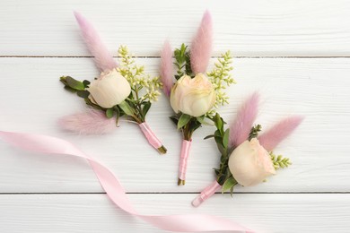 Photo of Small stylish boutonnieres and ribbon on white wooden table, flat lay