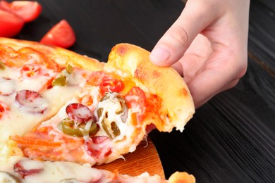 Photo of Woman taking piece of delicious pizza Diablo at black wooden table, closeup