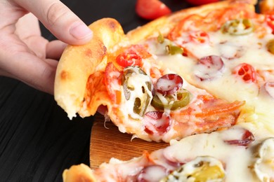 Photo of Woman taking piece of delicious pizza Diablo at black wooden table, closeup