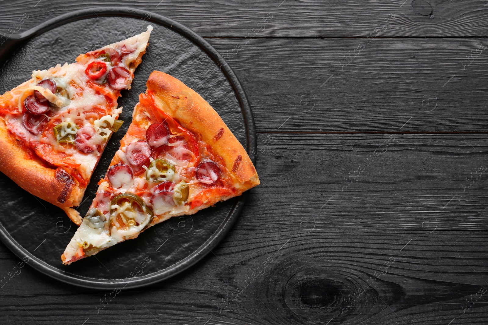 Photo of Board with pieces of delicious pizza Diablo on black wooden table, top view. Space for text