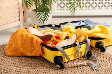 Photo of Open suitcase with traveler's belongings on floor indoors