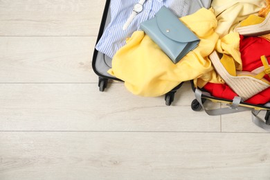 Photo of Open suitcase with traveler's belongings on floor, top view. Space for text