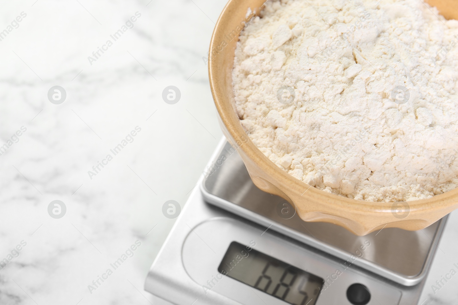 Photo of Kitchen scale with bowl of flour on white marble table, above view. Space for text