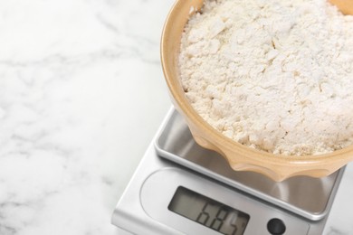 Kitchen scale with bowl of flour on white marble table, above view. Space for text