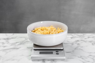 Photo of Kitchen scale with bowl of pasta on white marble table