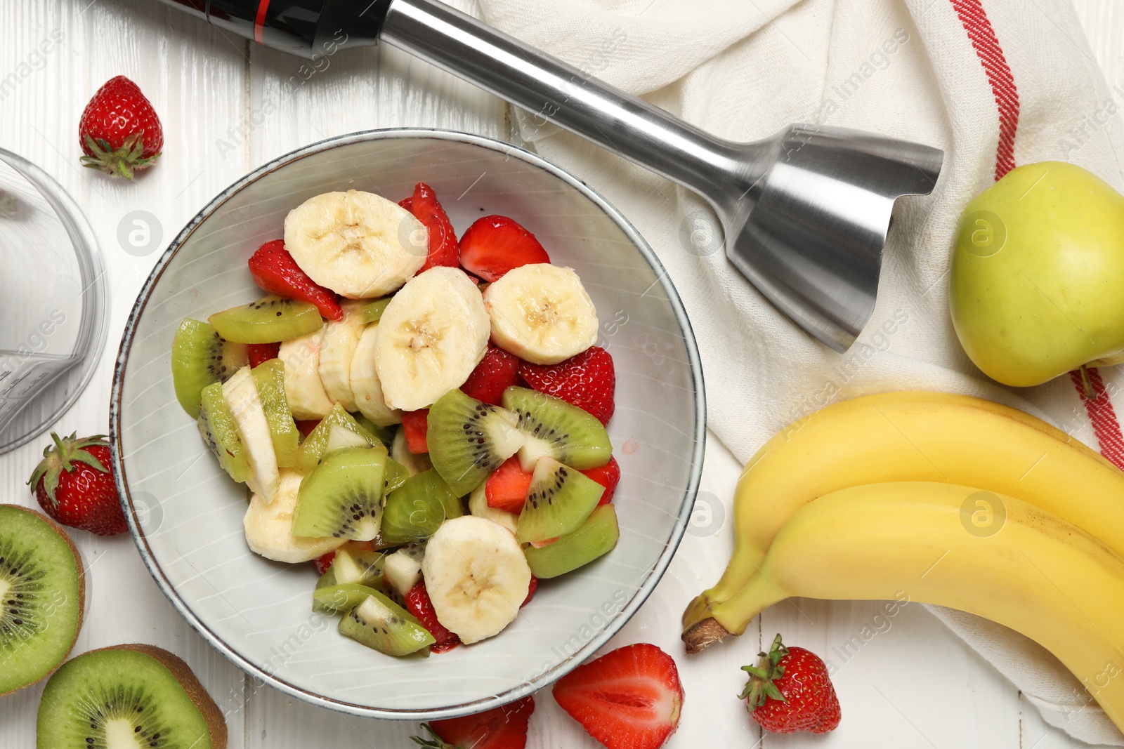 Photo of Hand blender kit, fresh fruits and strawberries in bowl on white wooden table, flat lay