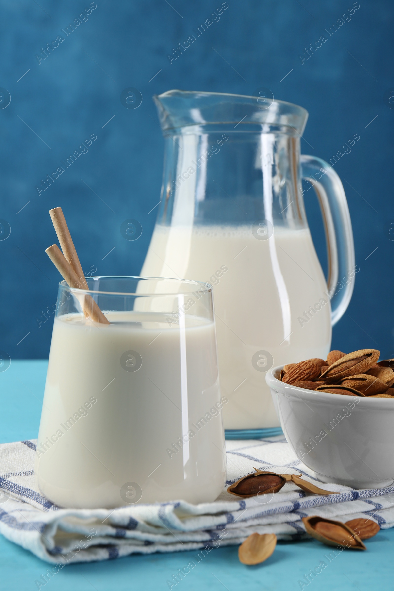 Photo of Glass of almond milk, jug and almonds on light blue wooden table