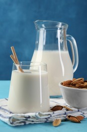 Glass of almond milk, jug and almonds on light blue wooden table