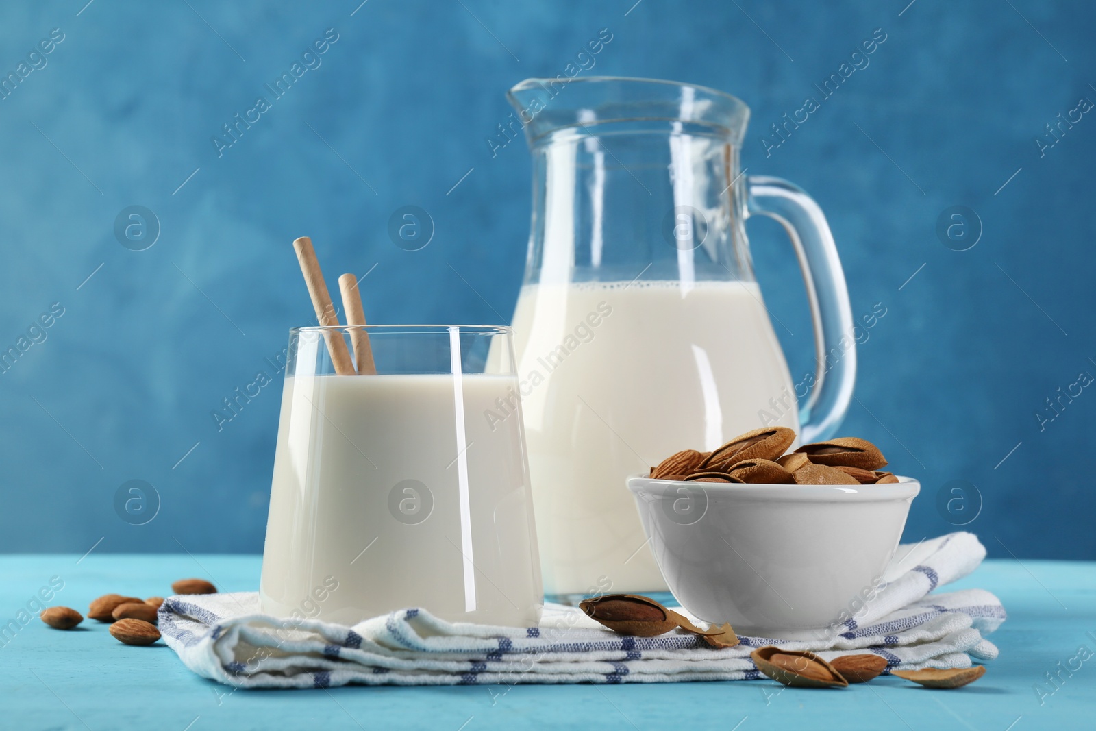 Photo of Glass of almond milk, jug and almonds on light blue wooden table