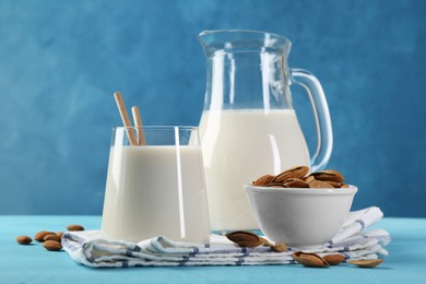 Glass of almond milk, jug and almonds on light blue wooden table