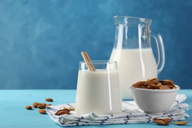 Photo of Glass of almond milk, jug and almonds on light blue wooden table, space for text