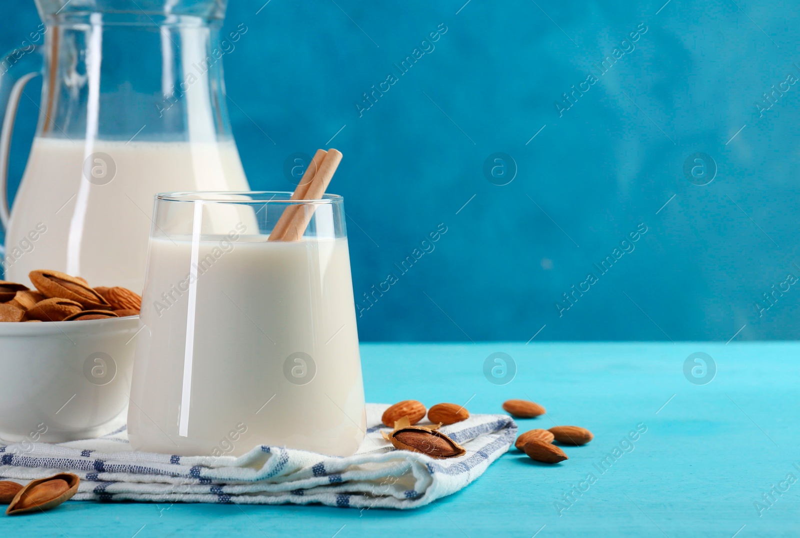 Photo of Glass of almond milk, jug and almonds on light blue wooden table, space for text