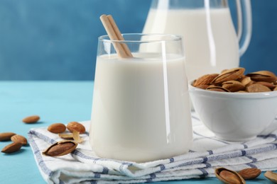 Photo of Glass of almond milk, jug and almonds on light blue wooden table, closeup