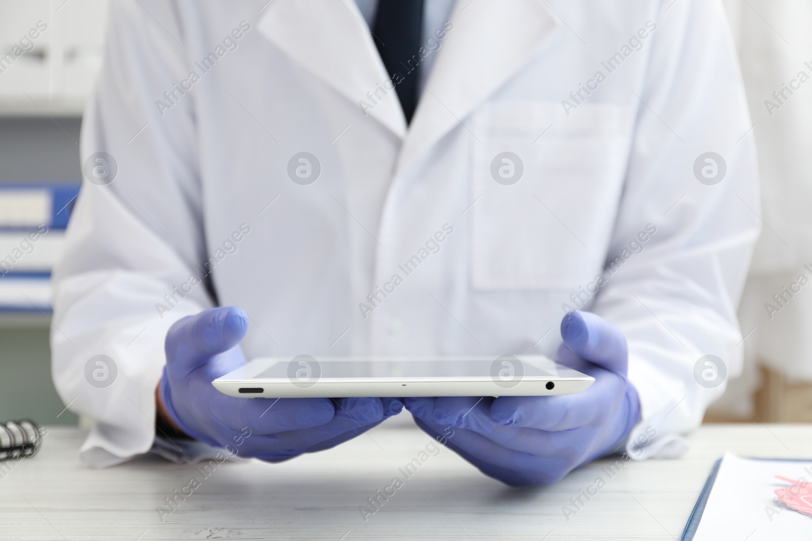 Photo of Doctor with tablet at white table indoors, closeup