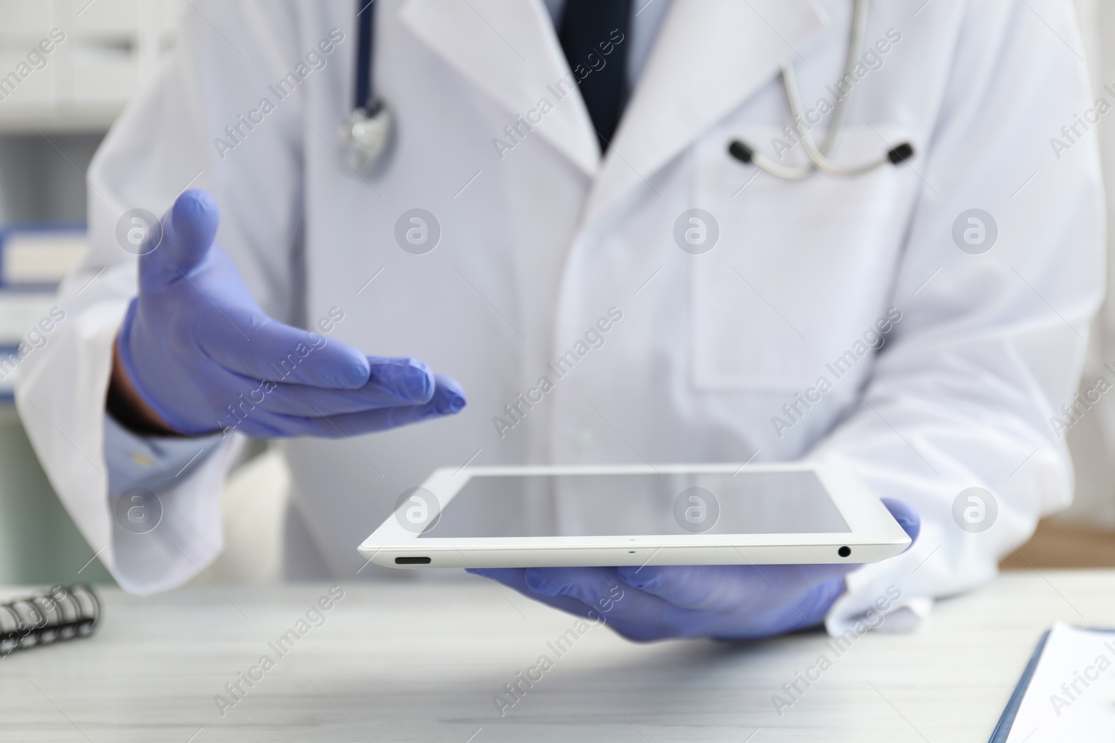 Photo of Doctor with tablet at white table indoors, closeup