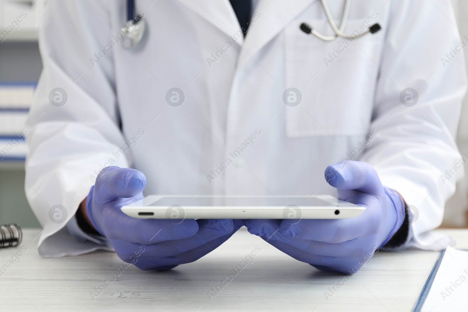 Photo of Doctor with tablet at white table indoors, closeup