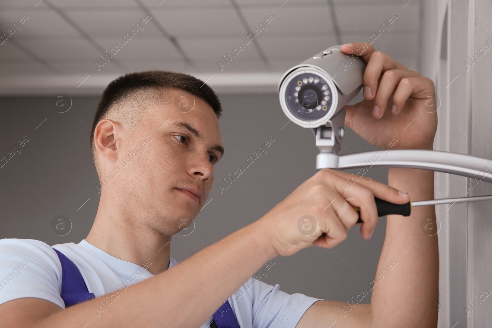 Photo of Technician with screwdriver installing CCTV camera on wall indoors