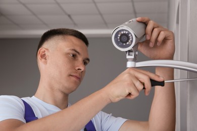 Photo of Technician with screwdriver installing CCTV camera on wall indoors