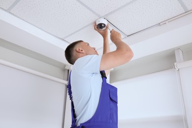 Photo of Technician with screwdriver installing CCTV camera on ceiling indoors