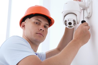 Technician with screwdriver installing CCTV camera on wall indoors