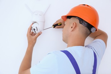 Technician with screwdriver installing CCTV camera on wall indoors, back view