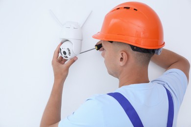 Photo of Technician with screwdriver installing CCTV camera on wall indoors, back view