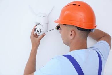 Technician with screwdriver installing CCTV camera on wall indoors, back view