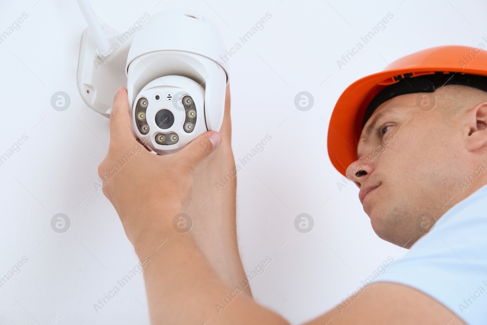 Photo of Technician installing CCTV camera on wall indoors, low angle view