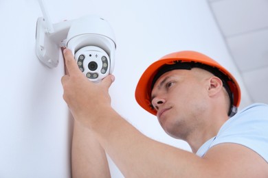 Technician installing CCTV camera on wall indoors, low angle view