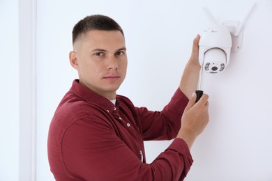 Technician with screwdriver installing CCTV camera on wall indoors