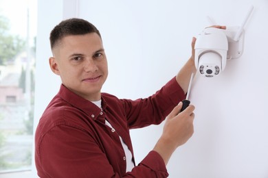 Technician with screwdriver installing CCTV camera on wall indoors