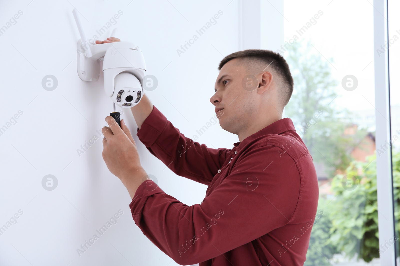 Photo of Technician with screwdriver installing CCTV camera on wall indoors