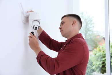 Technician with screwdriver installing CCTV camera on wall indoors