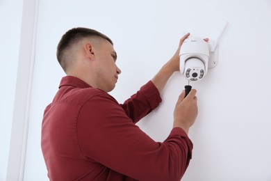 Technician with screwdriver installing CCTV camera on wall indoors