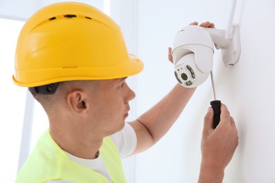 Technician with screwdriver installing CCTV camera on wall indoors, closeup